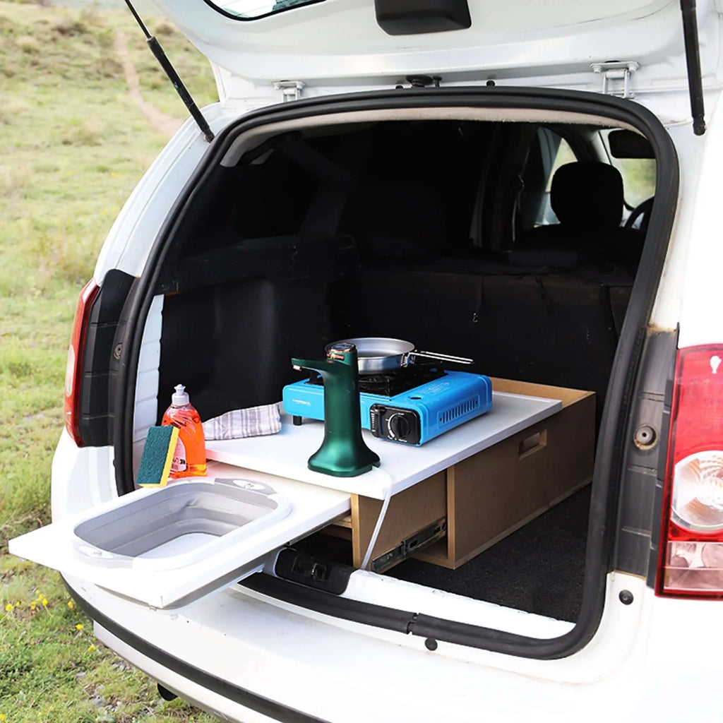 Car trunk transformed into a wooden mobile kitchen with a stove, sink, and storage, ideal for camping and road trips.