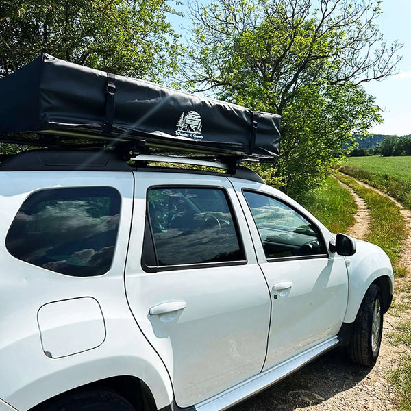 SUV blanc avec une couverture de tente en PVC pour 3 à 5 personnes, protégeant contre les intempéries sur une route de campagne, arbres en arrière-plan.
