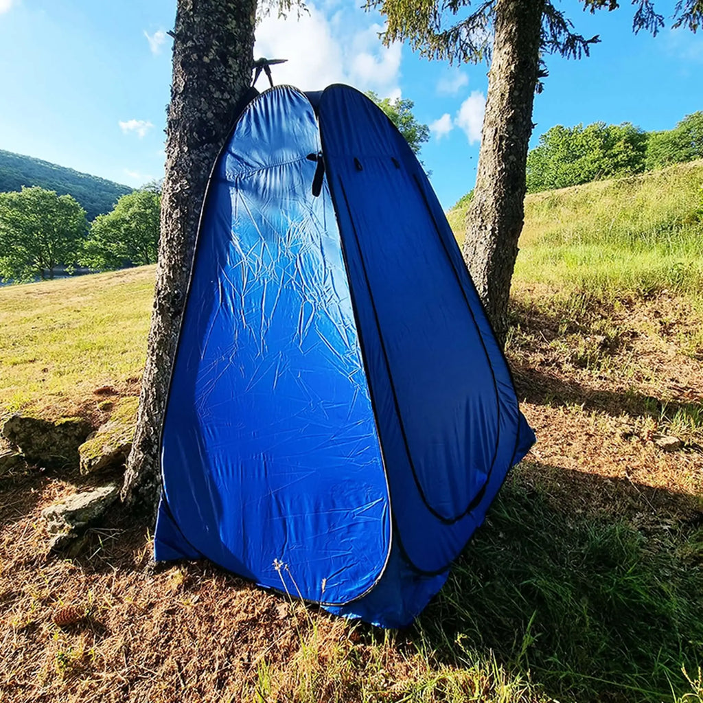 Tente de douche extérieure pliante bleue installée dans une forêt, offrant de l'intimité pour prendre des douches, se changer et plus encore lors des aventures.